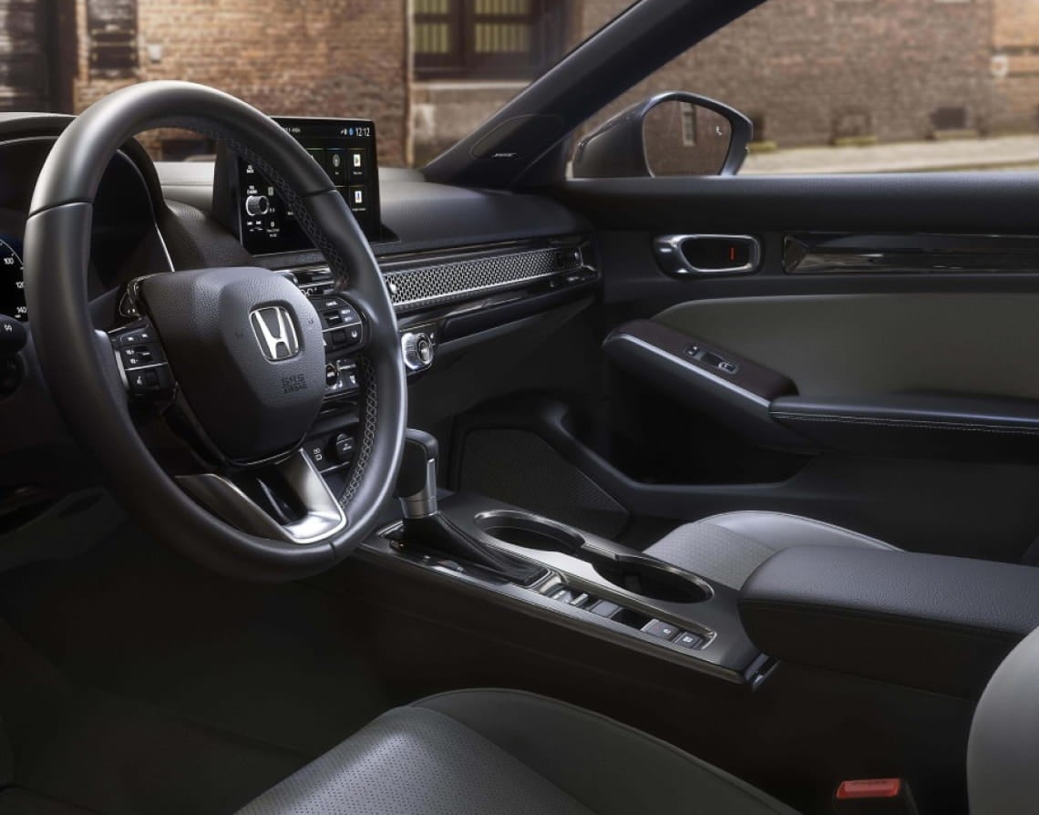 Interior view of the Honda Civic Sedan featuring the steering wheel, digital display, center console, and front passenger area.
