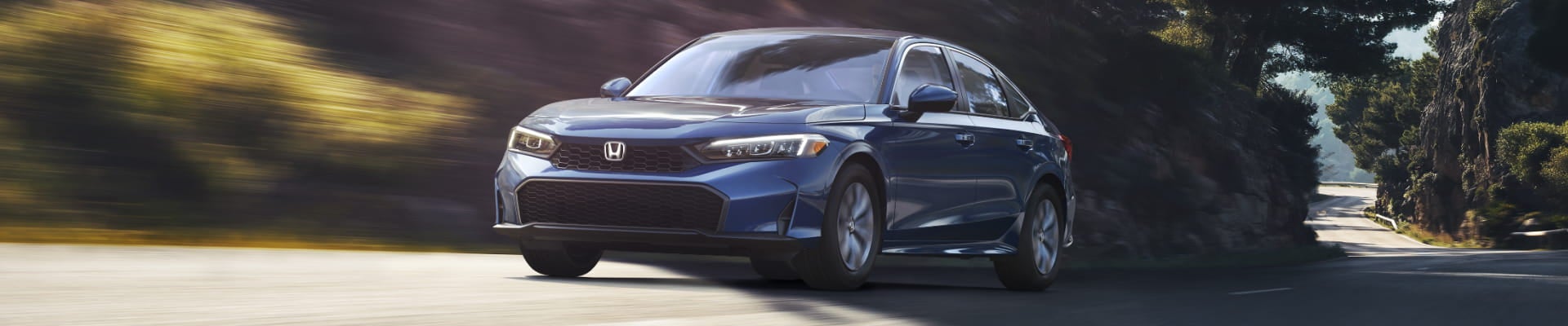 Blue Honda Civic Sedan driving on a winding road through a wooded landscape, shown from a front three-quarter angle.
