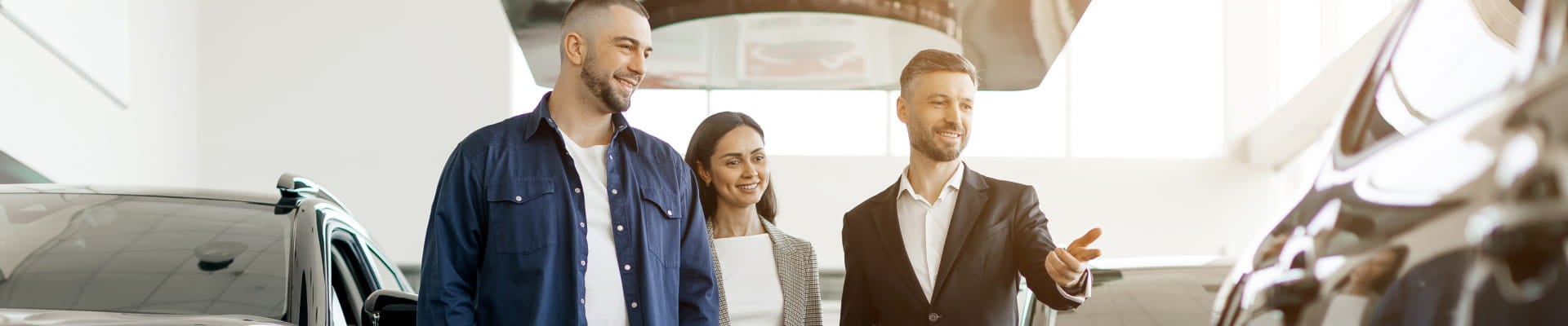 Car salesperson showing a vehicle to two customers inside a dealership showroom.